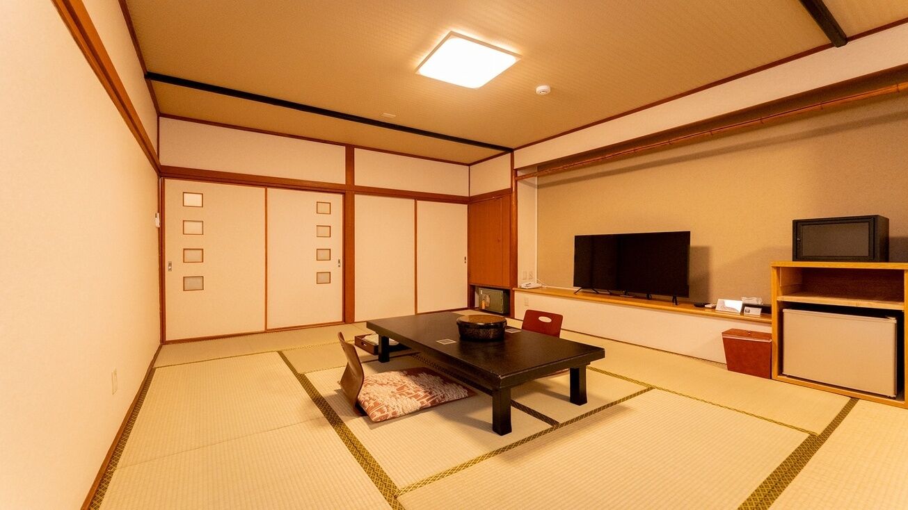 Perinteinen japanilaistyylinen huone, jossa on tatamimatto, matala pöytä, televisio ja pieni hylly.