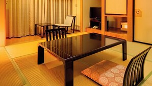 Una habitación tradicional japonesa con suelo de tatami, una mesa baja, sillas, un televisor y una puerta corredera.