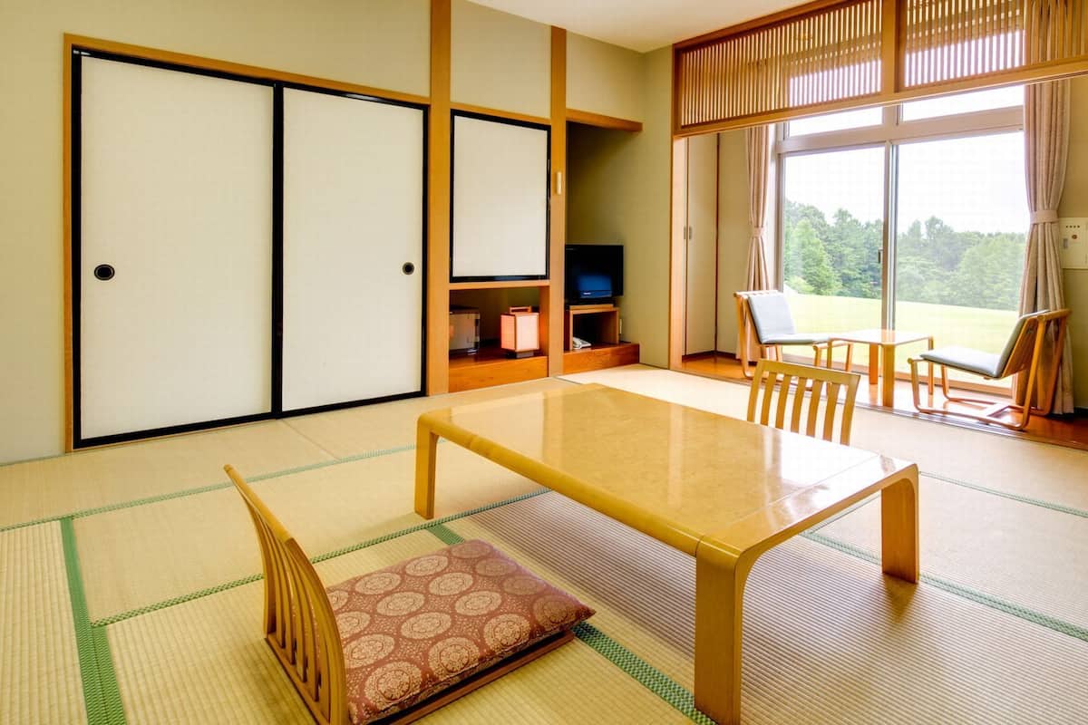 A traditional Japanese room with tatami flooring, a low table, chairs, a television, and sliding doors.