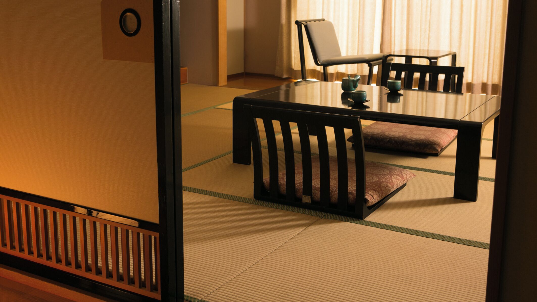 Um espaço com tatames, uma mesa baixa e cadeiras, um conjunto de chá e um separador shoji.