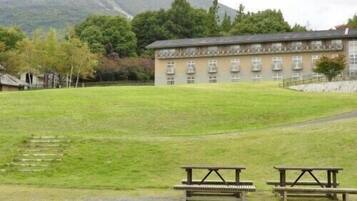 Un edificio con una larga hilera de ventanas, un césped y dos mesas de picnic.