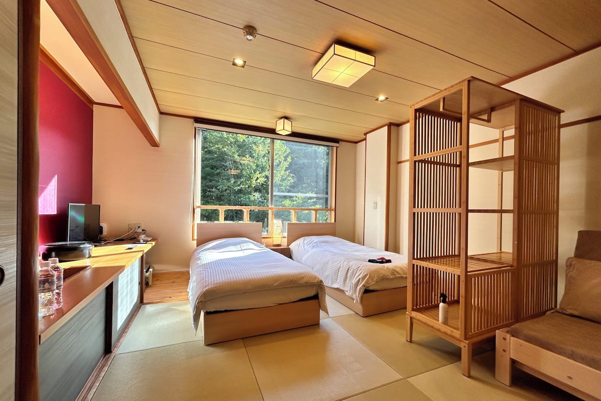 Una habitación de estilo japonés tradicional con suelo de tatami, dos camas, un escritorio con computadora y un panel de madera corredera.