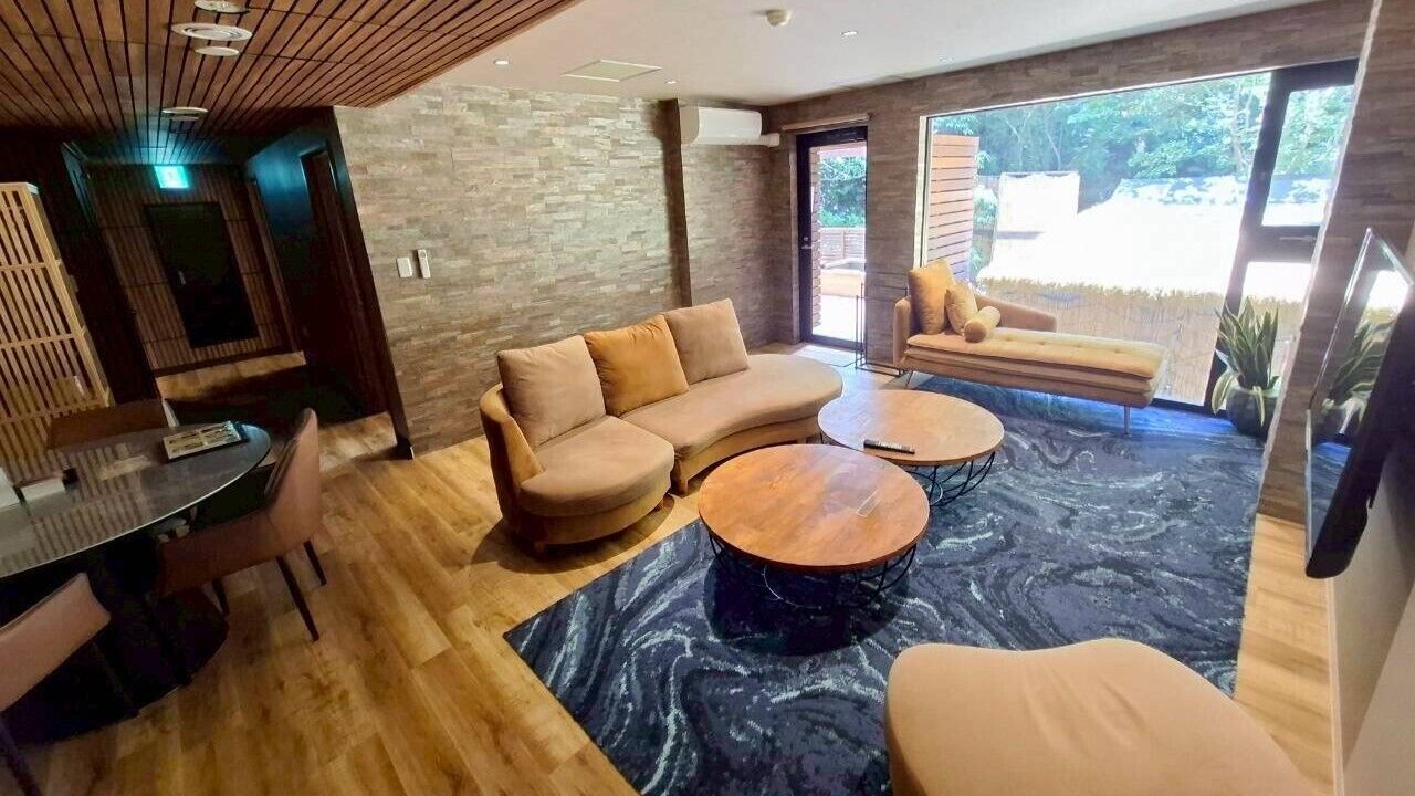 Ein modernes Wohnzimmer mit einer Eckcouch, runden Couchtischen und einem Essbereich mit Tisch und Stühlen.