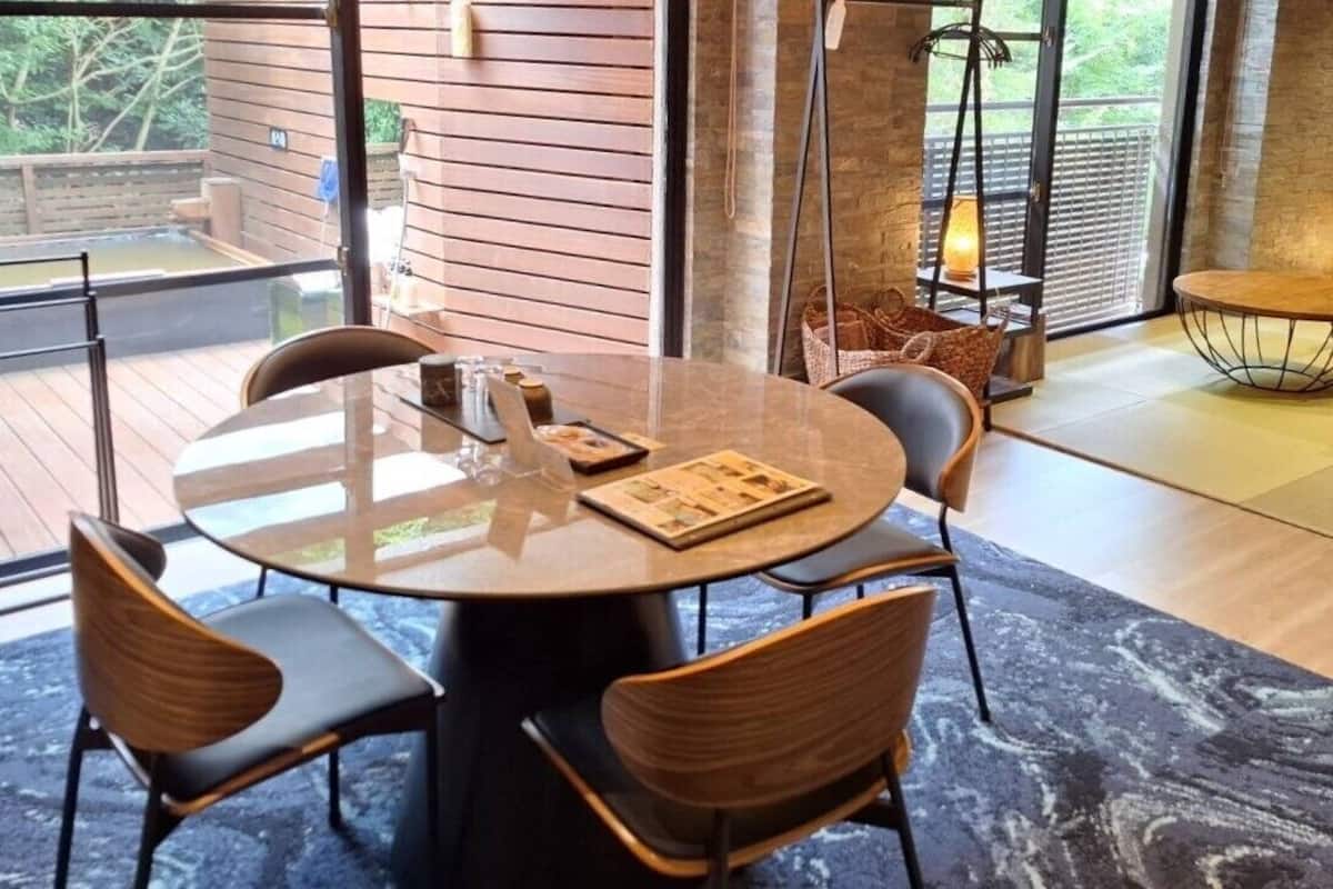 Un interior moderno con una mesa redonda, sillas, un sofá y vistas a un área de aguas termales.