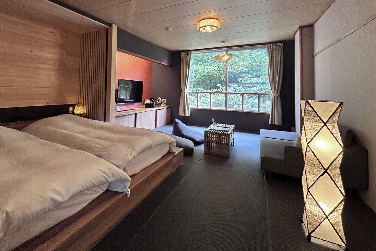 Un dormitorio con una cama grande, un escritorio, una silla y una ventana que da a vistas de árboles.