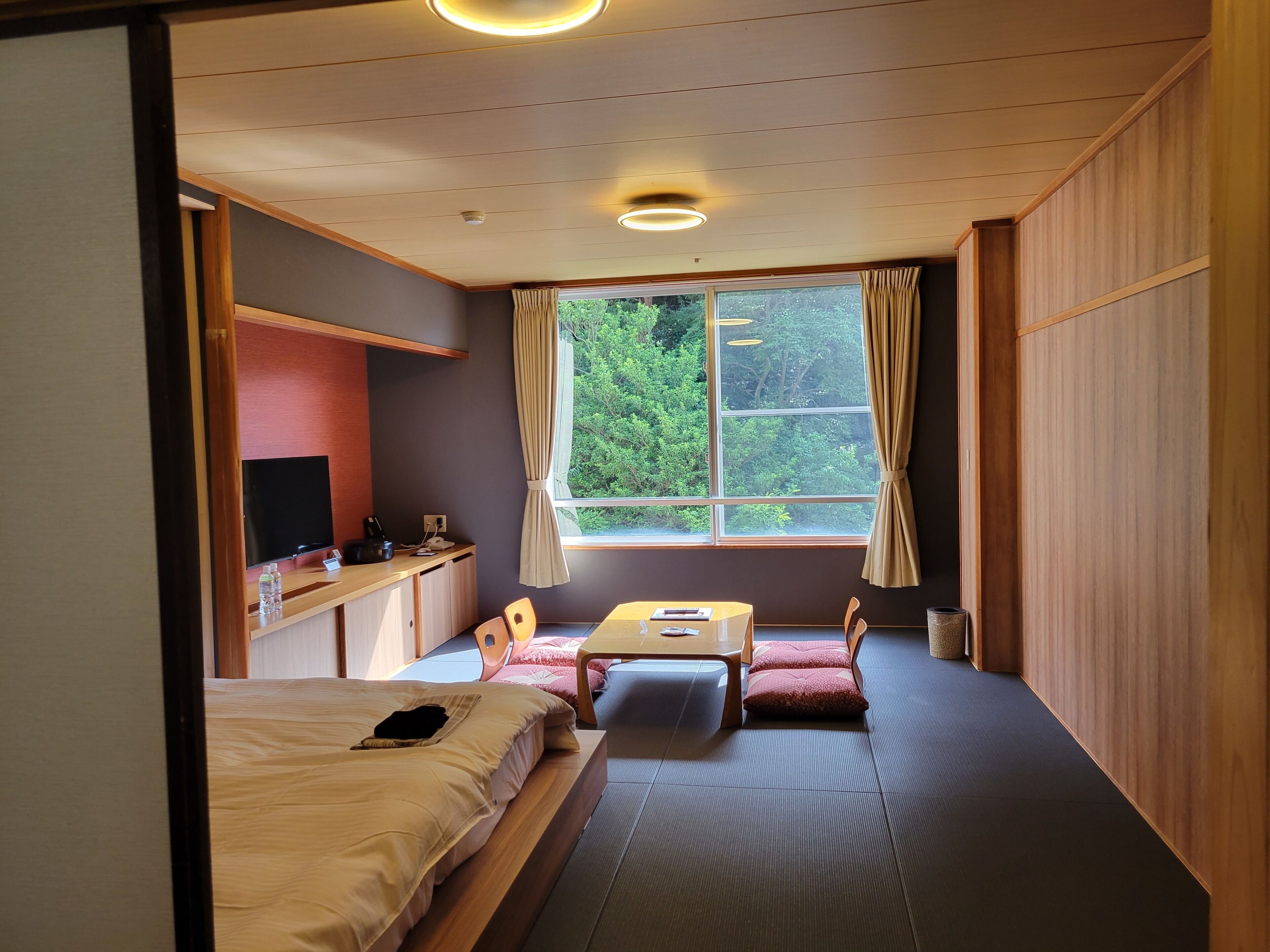 Ein Zimmer mit einem Bett, einem Schreibtisch, einem Stuhl, einem kleinen Tisch und einem Fenster mit Vorhängen.