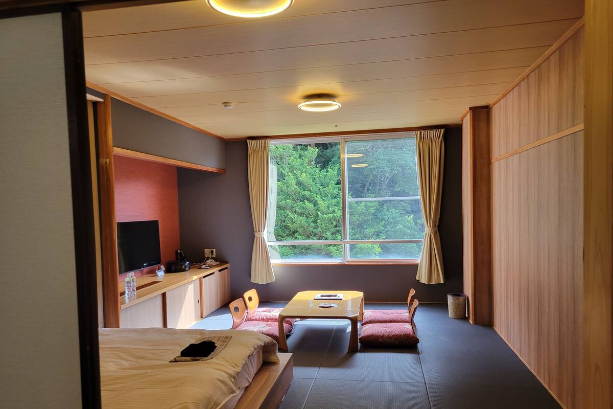 Una habitación con cama, escritorio, silla, mesita y ventana con cortinas.