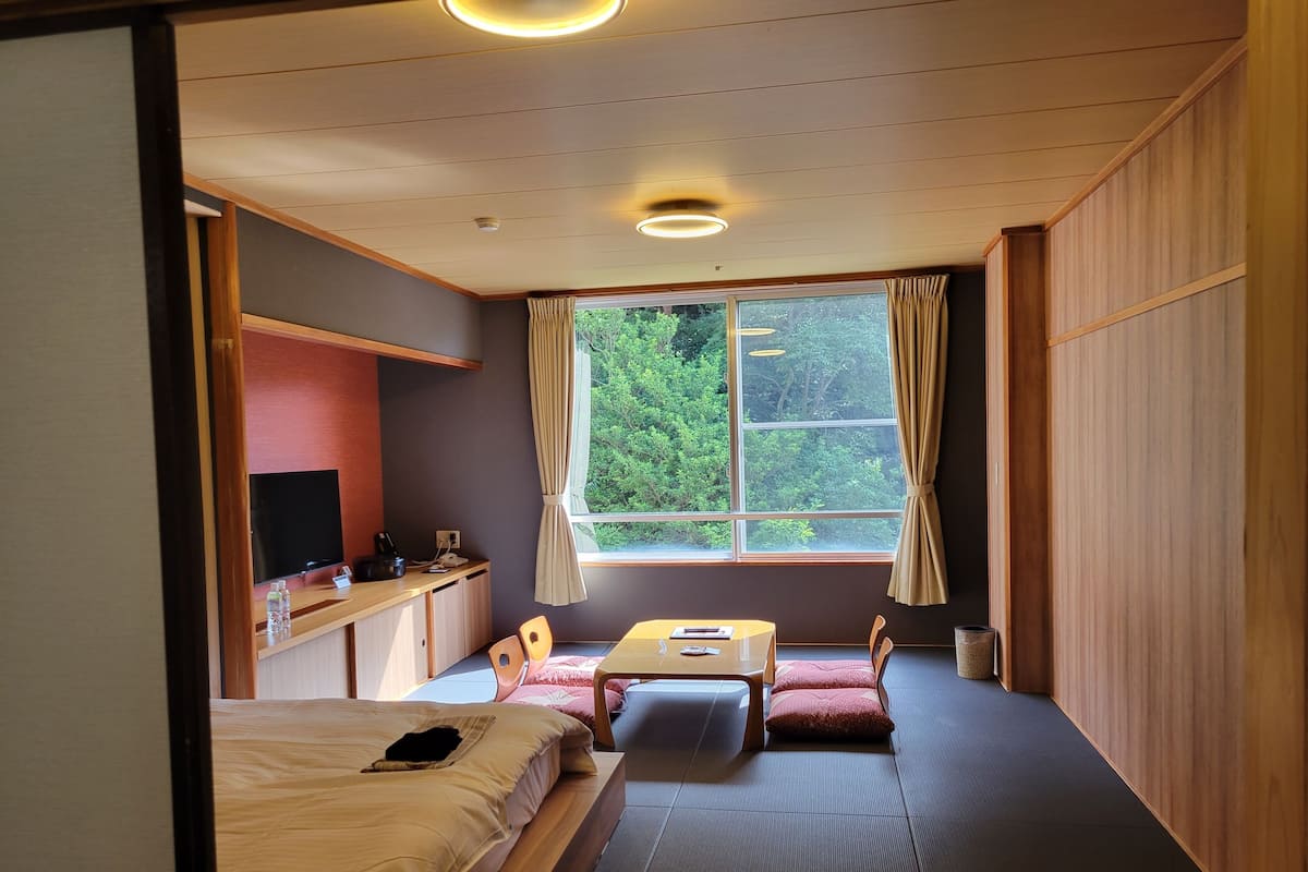 Ein Zimmer mit einem Bett, einem Schreibtisch, einem Stuhl, einem kleinen Tisch und einem Fenster mit Vorhängen.