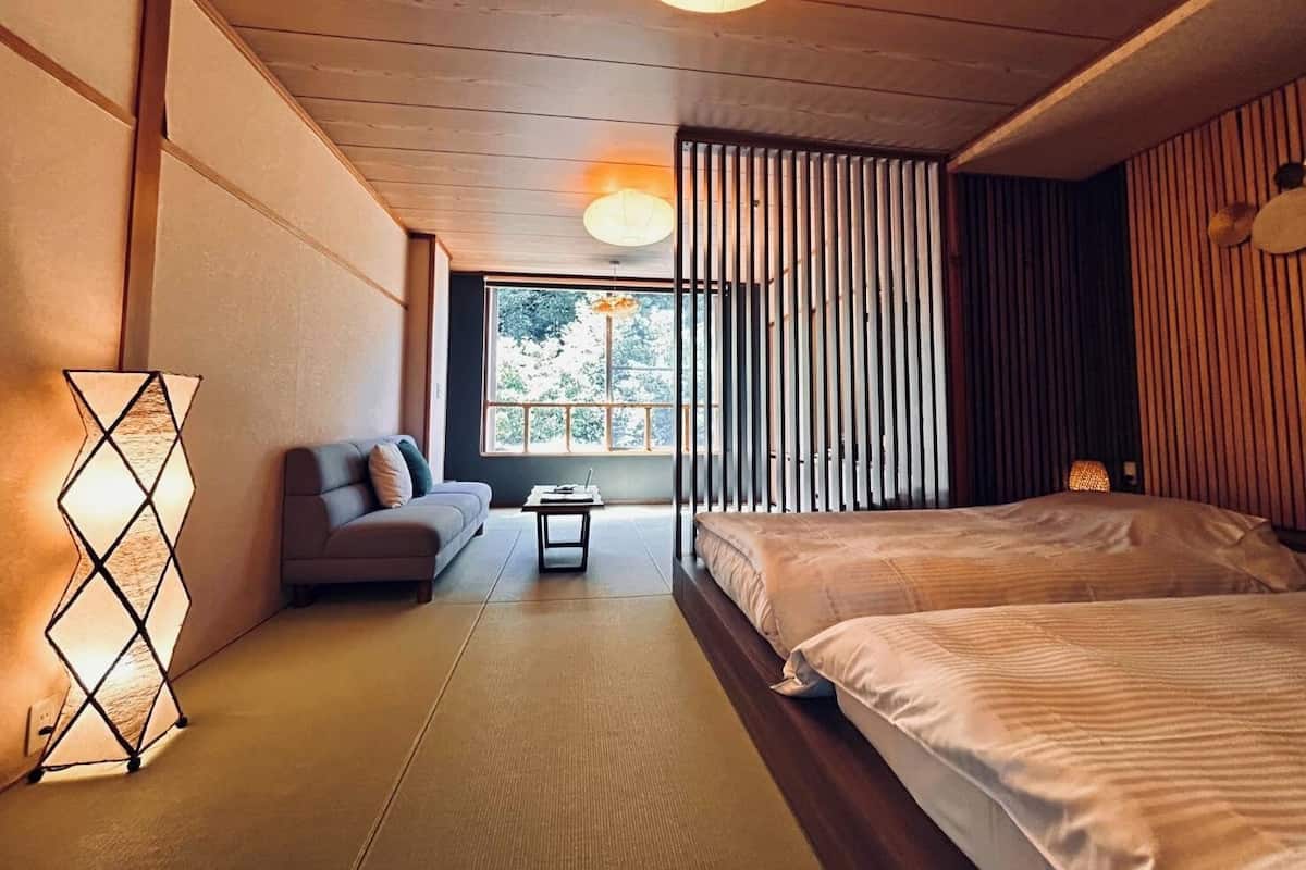 Una habitación con sofá, cama, una mesita y ventana con persianas verticales.