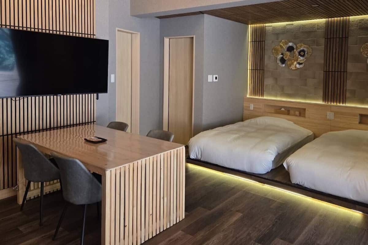 Una habitación de hotel moderna con un escritorio de madera, dos camas, un televisor de pantalla plana y decoración en la pared.