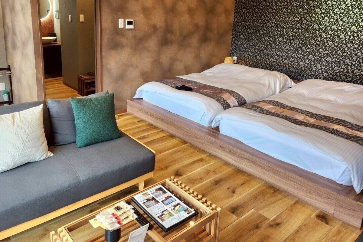 Una habitación de hotel moderna con un sofá, dos camas, una mesita de centro de madera y una mesita auxiliar pequeña.