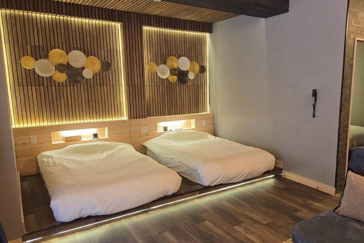 Una habitación con dos camas, techo de madera, pared con lámparas circulares y pared de ladrillo.