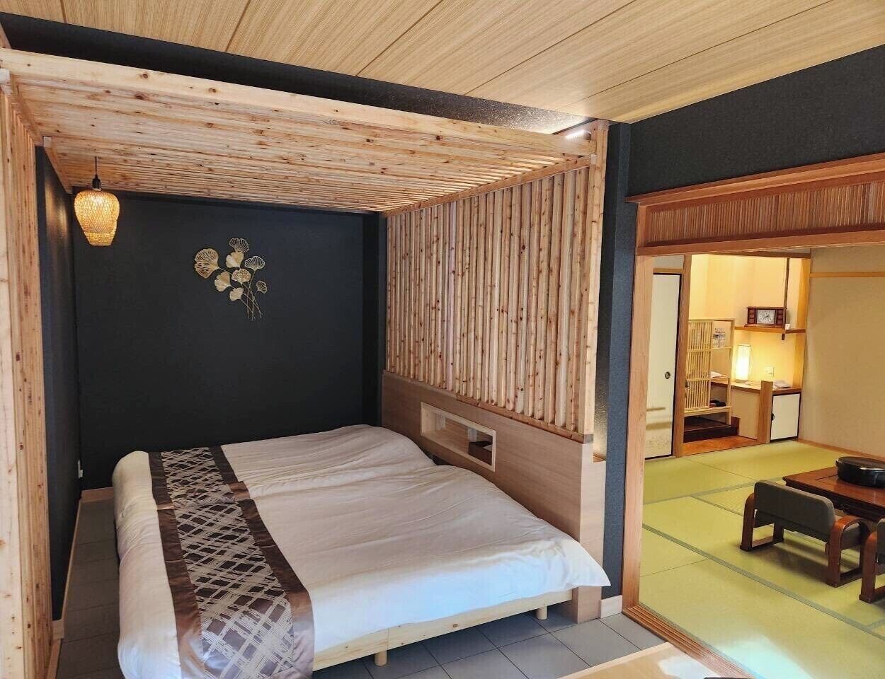 Ein Zimmer mit einem Bett, einem hölzernen Kopfteil, einer Pendelleuchte und einem traditionellen Tisch im japanischen Stil mit Stühlen.