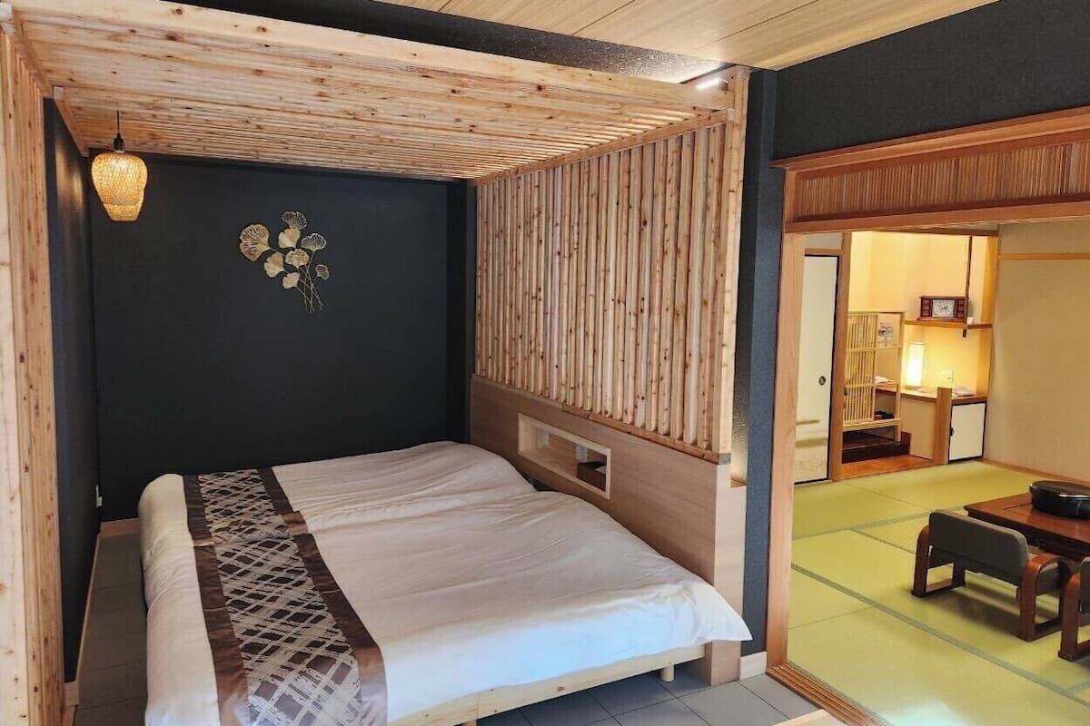 Una habitación con una cama, cabecera de madera, lámpara colgante y una mesa tradicional al estilo japonés con sillas.