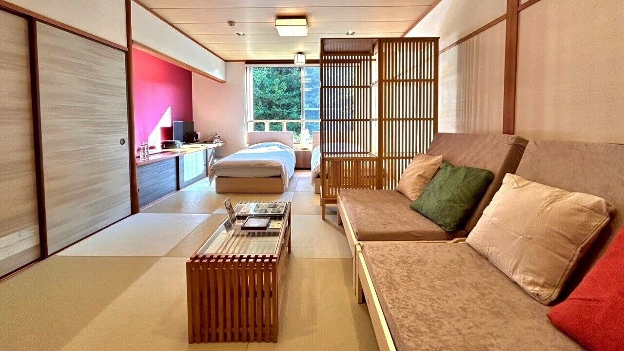 Ein traditioneller japanischer Raum mit Tatami-Böden, einem niedrigen Holztisch, einer Couch mit Kissen und verschiebbaren Türen.
