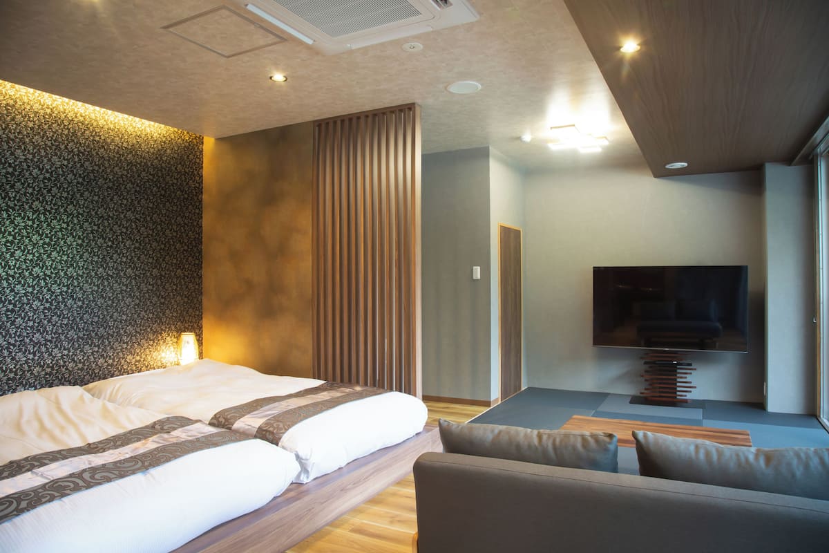 Una habitación de hotel moderna con una cama grande, un sofá, un televisor y un panel de pared de madera.