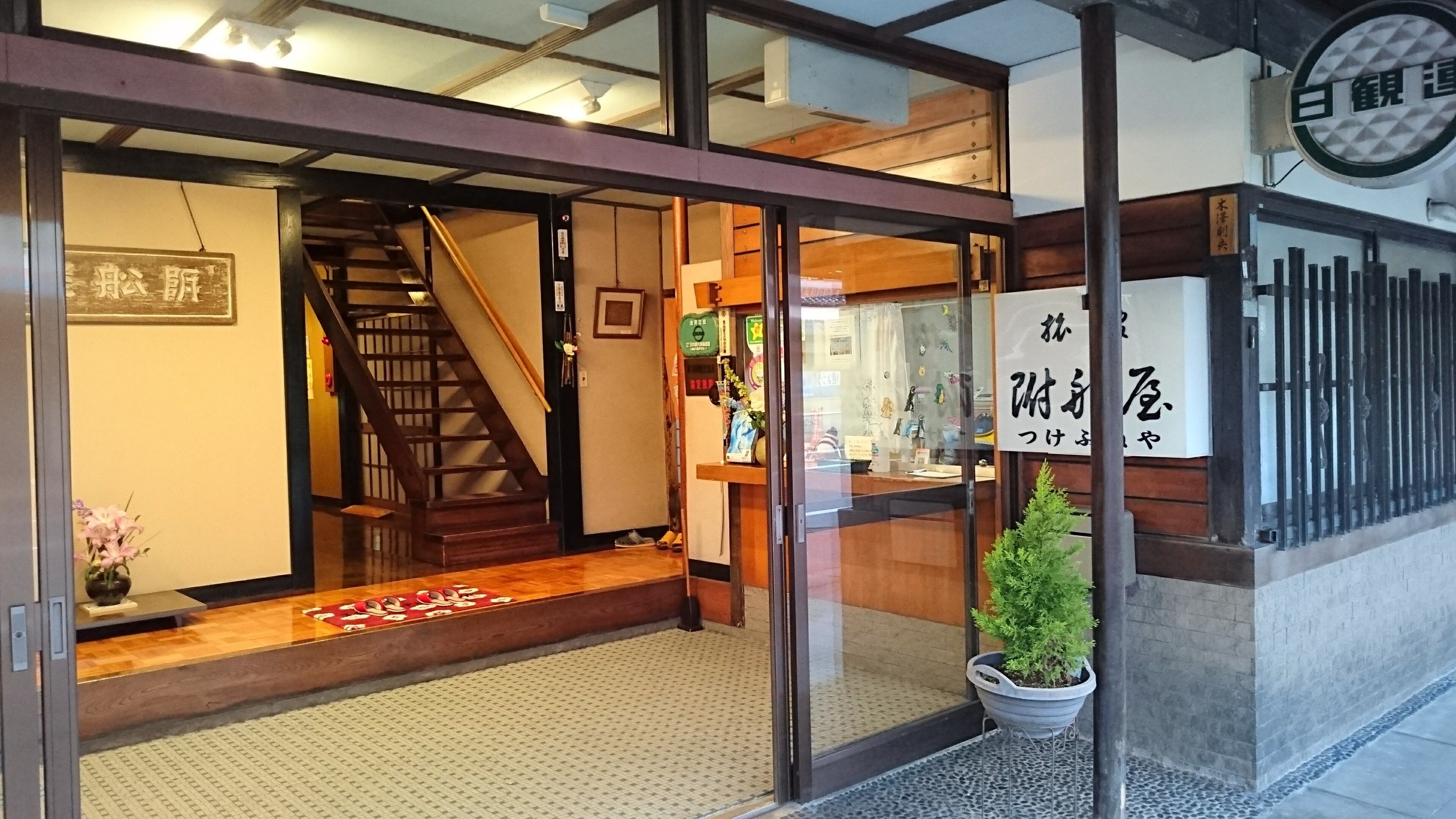 Une entrée d’immeuble avec un escalier en bois, un pot de fleurs et une enseigne avec des caractères japonais.