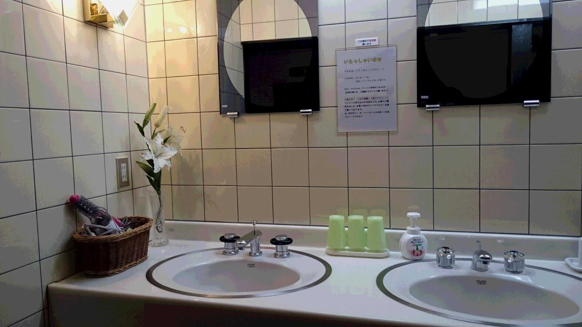 Une salle de bain avec deux lavabos, un miroir et un panneau affichant du texte en japonais.