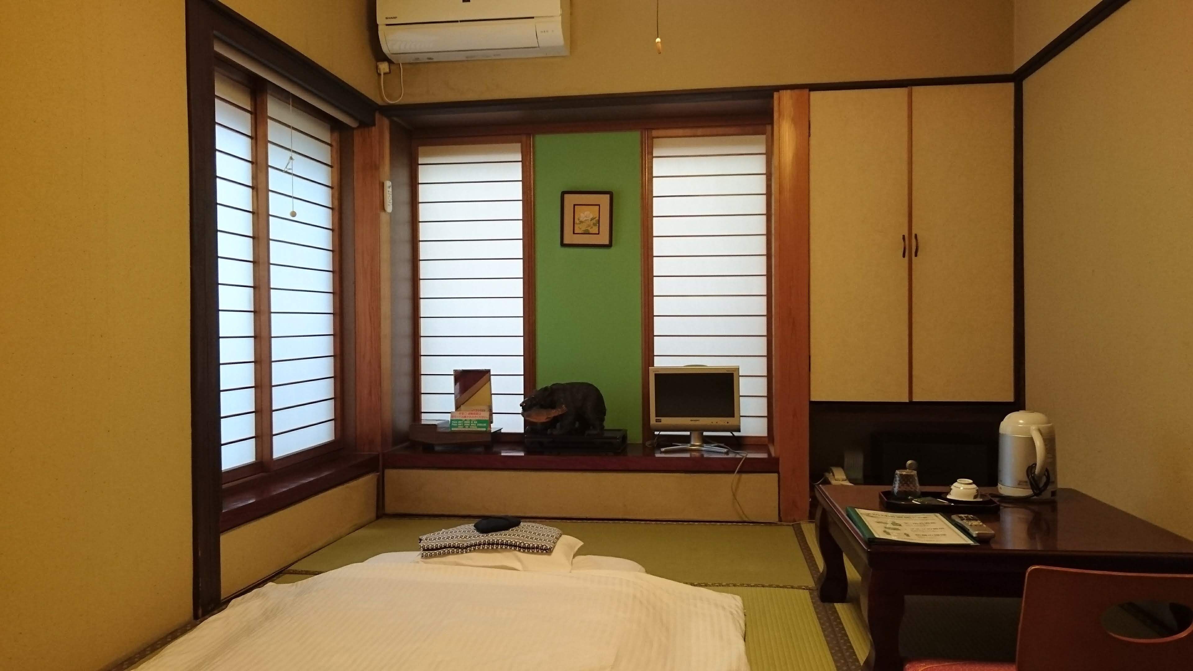 A hotel room with a bed, a desk with a computer, a chair, and a window with blinds.