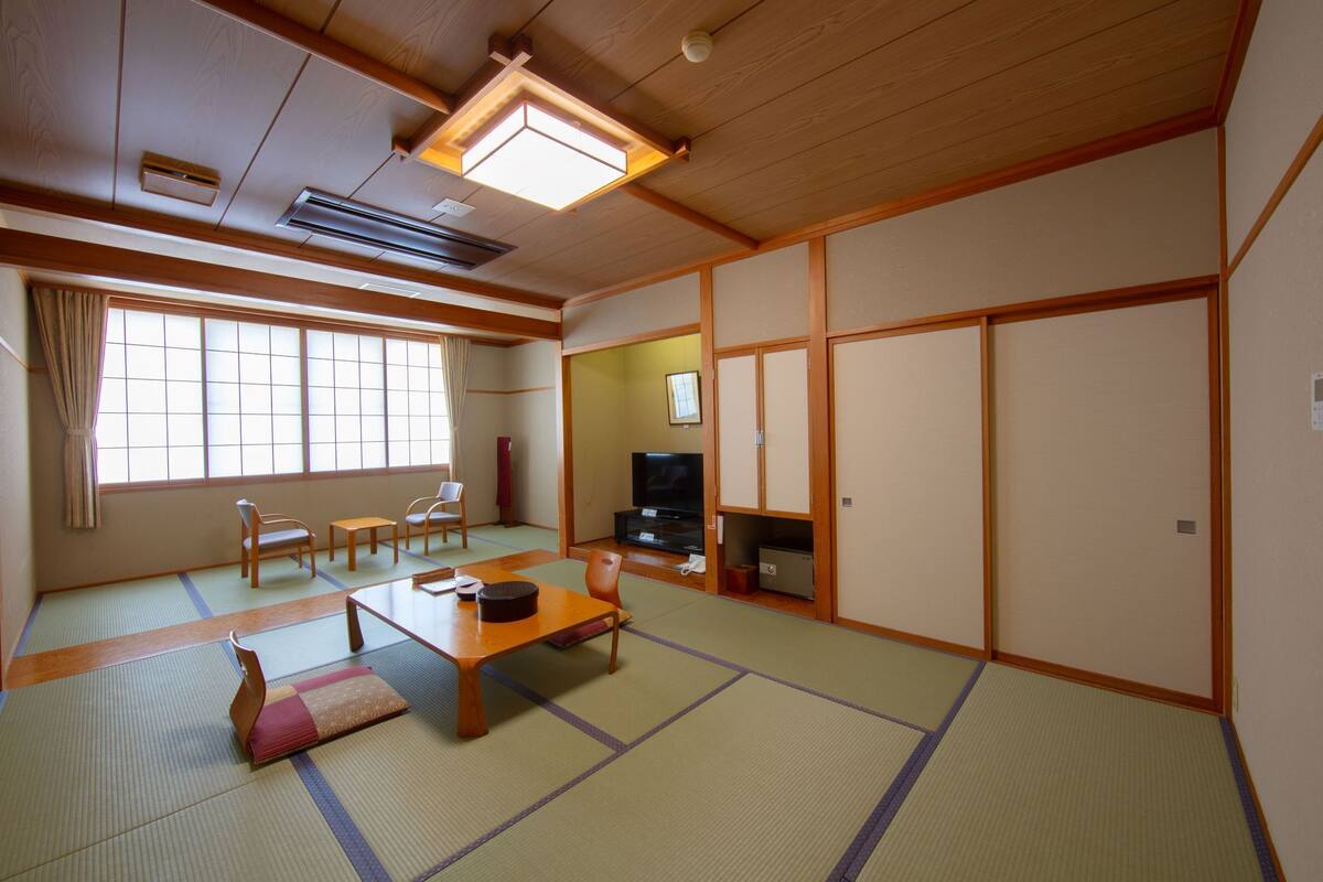 Um quarto japonês tradicional com tatames, uma mesa baixa, cadeiras, uma televisão e portas deslizantes.