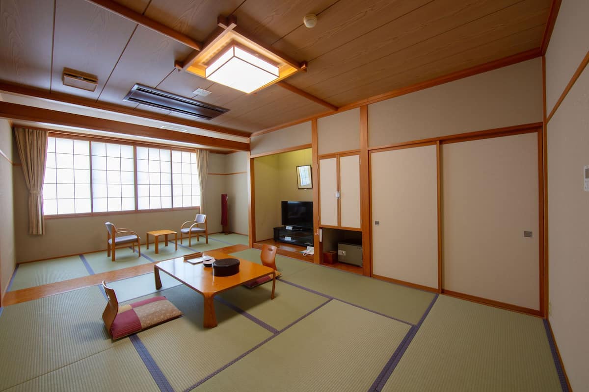 Ein traditioneller japanischer Raum mit Tatami-Bodenbelag, einem niedrigen Tisch, Stühlen, einem Fernseher und Schiebetüren.