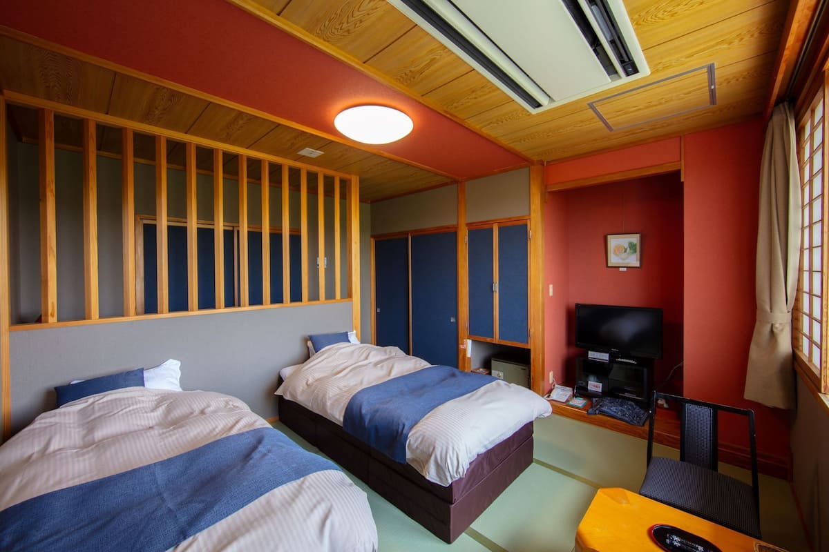 Quarto com duas camas, televisão, escrivaninha e uma cadeira.