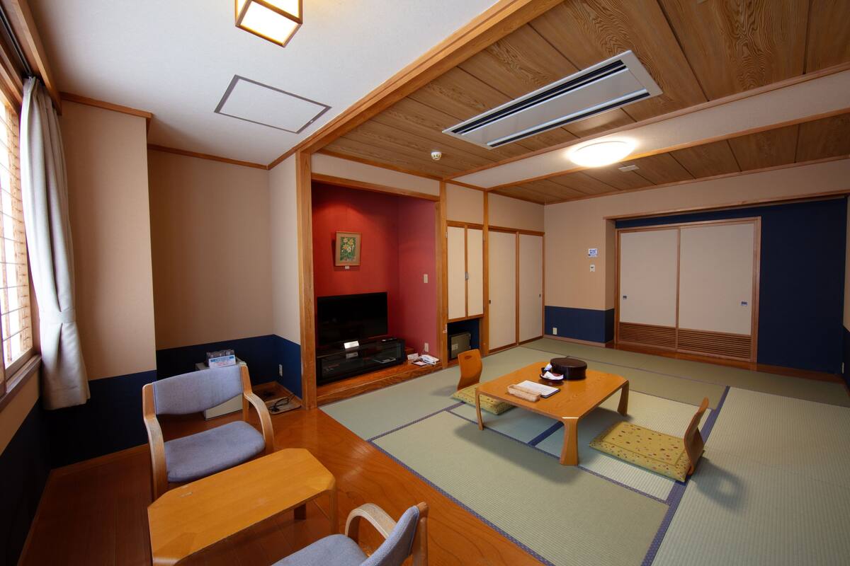 Um quarto japonês tradicional com tatames, televisão, sofá e porta deslizante.