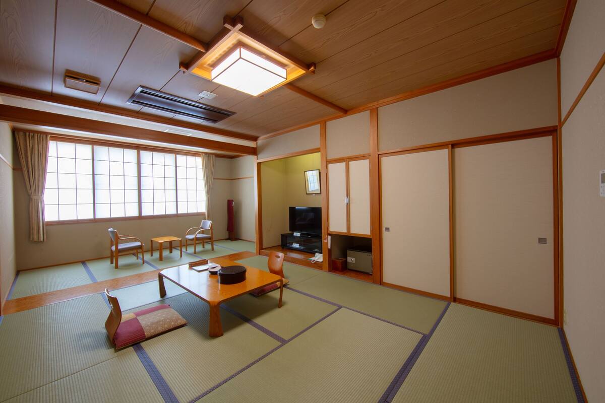 Um quarto japonês tradicional com tatames, uma mesa baixa, cadeiras, uma televisão e portas deslizantes.