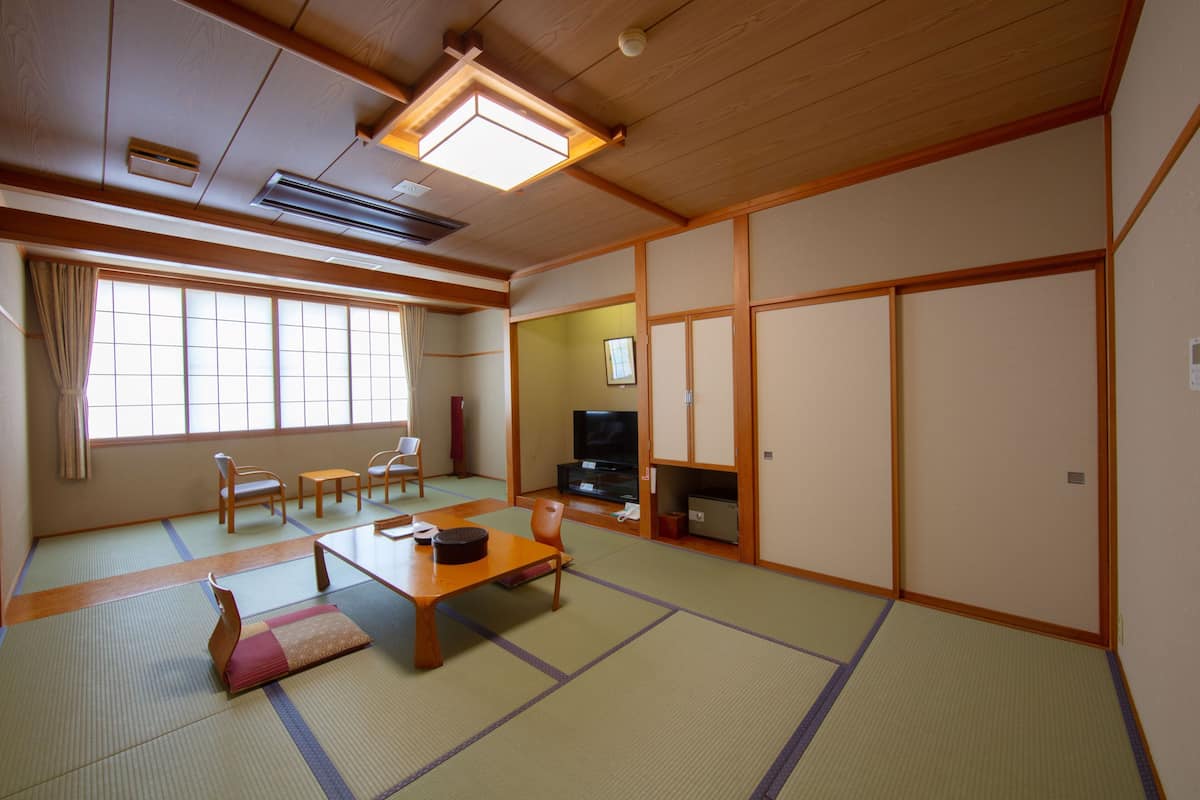 Ein traditioneller japanischer Raum mit Tatami-Boden, einem niedrigen Tisch, Stühlen, einem Fernseher und Schiebetüren.