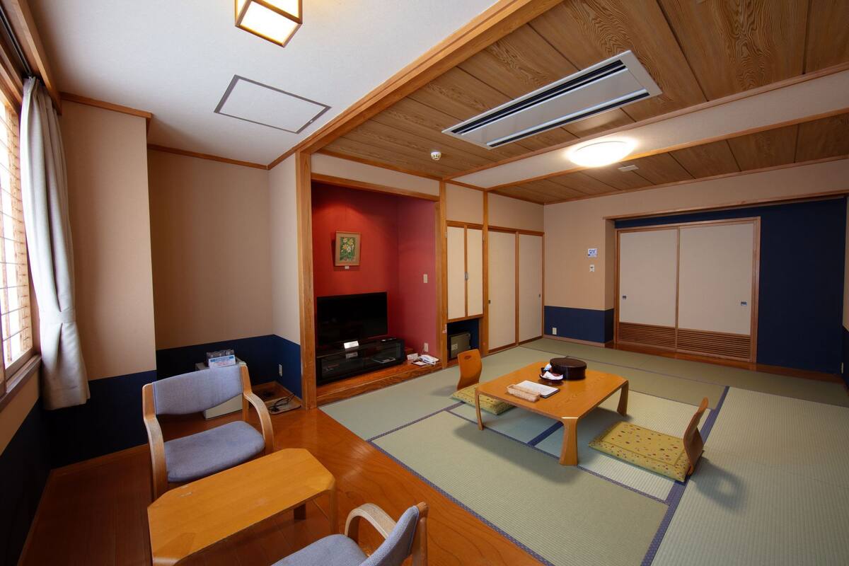 Um quarto japonês tradicional com tatames, televisão, sofá e porta deslizante.