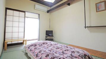 Um quarto japonês tradicional com tatames, futon, televisão sobre suporte e porta deslizante.