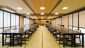 Une salle de conférence dotée de longues tables et de chaises, de grandes fenêtres et d’un plafond en bois.