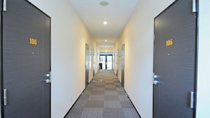 Un couloir d’hôtel avec les portes numérotées 105 et 106, un sol recouvert de moquette et un luminaire au plafond.