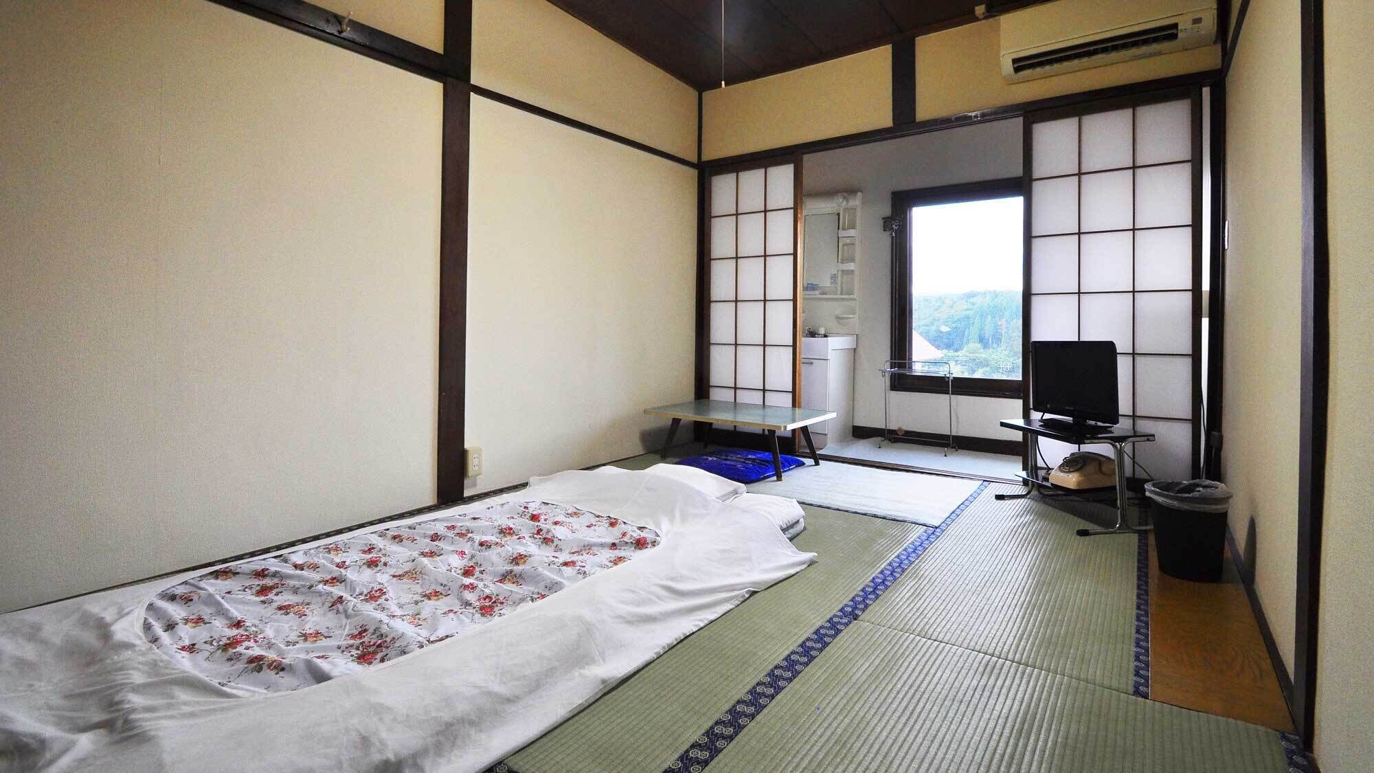 A traditional Japanese room with tatami flooring, a futon bed, a television, and a view of a forest through a shoji screen.