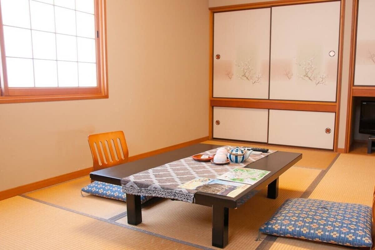 Una habitación japonesa tradicional con suelo de tatami, una mesa baja con cojines, un televisor y puertas correderas con diseños florales.