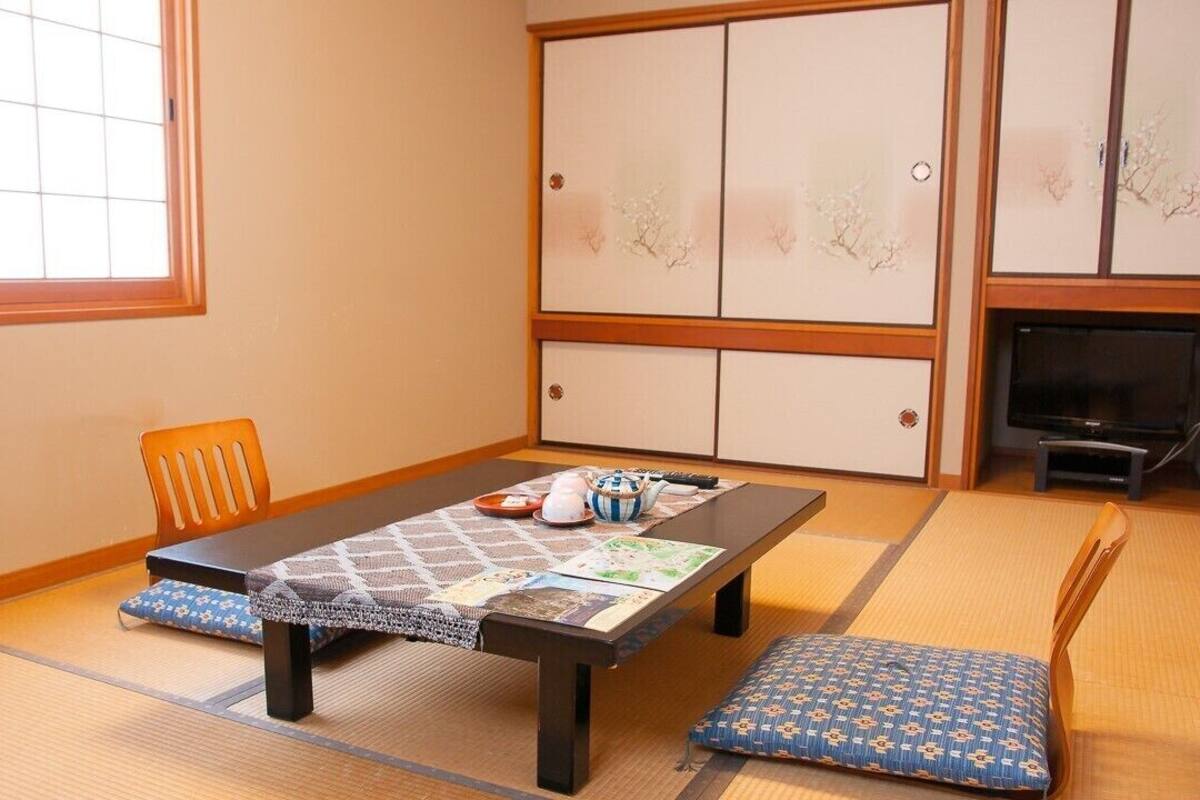 Una habitación con suelo de tatami, una mesa baja, cojines, un televisor y puertas correderas.