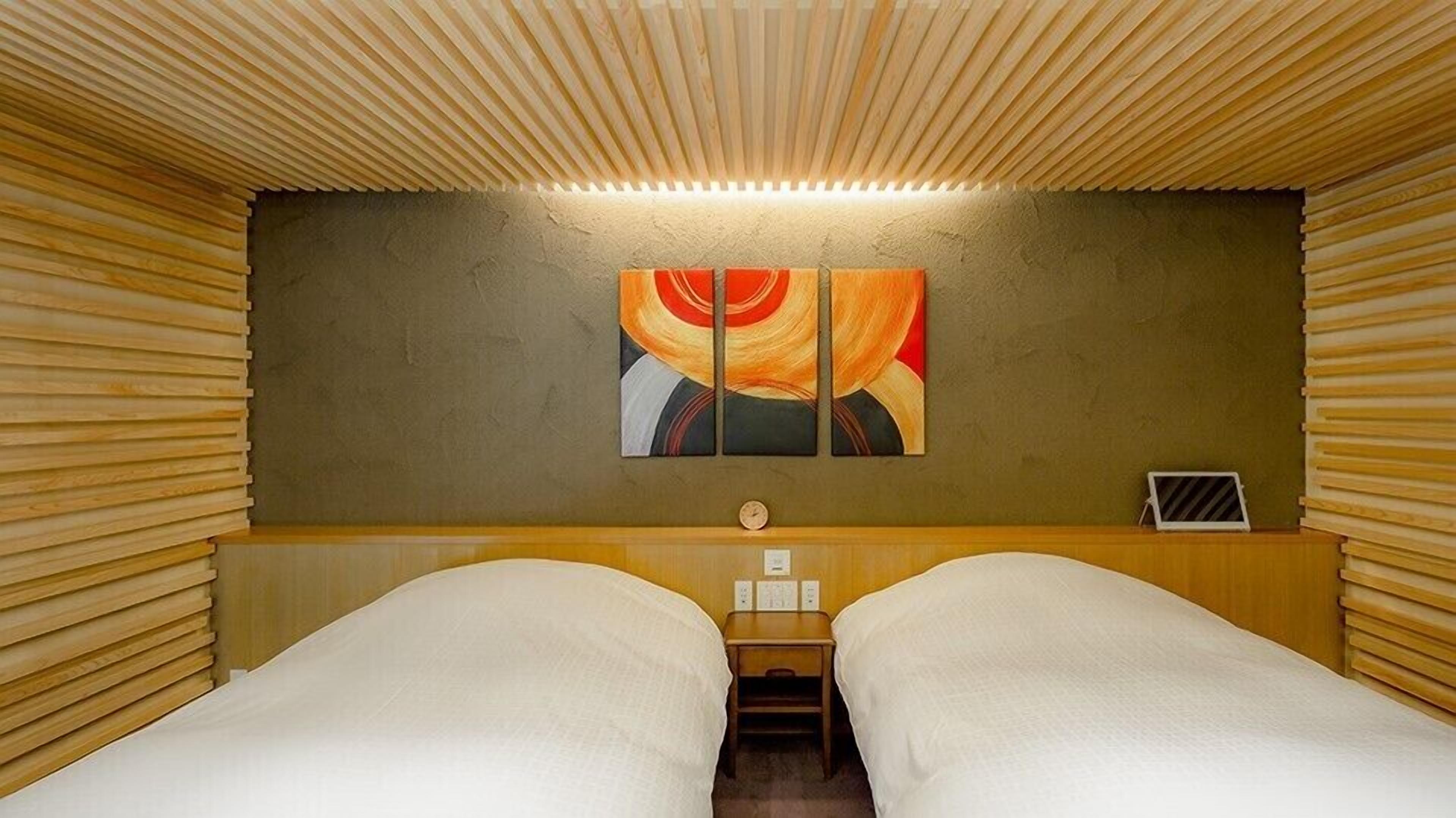 Een kamer met twee bedden, een houten lattenplafond, een wandklok en een schilderij.