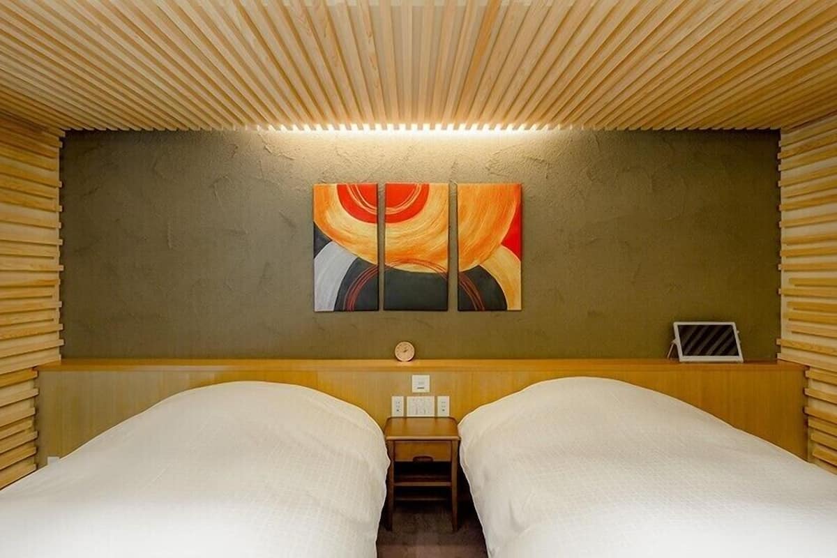 Quarto com duas camas, teto de ripas de madeira, relógio fixado na parede e um quadro.
