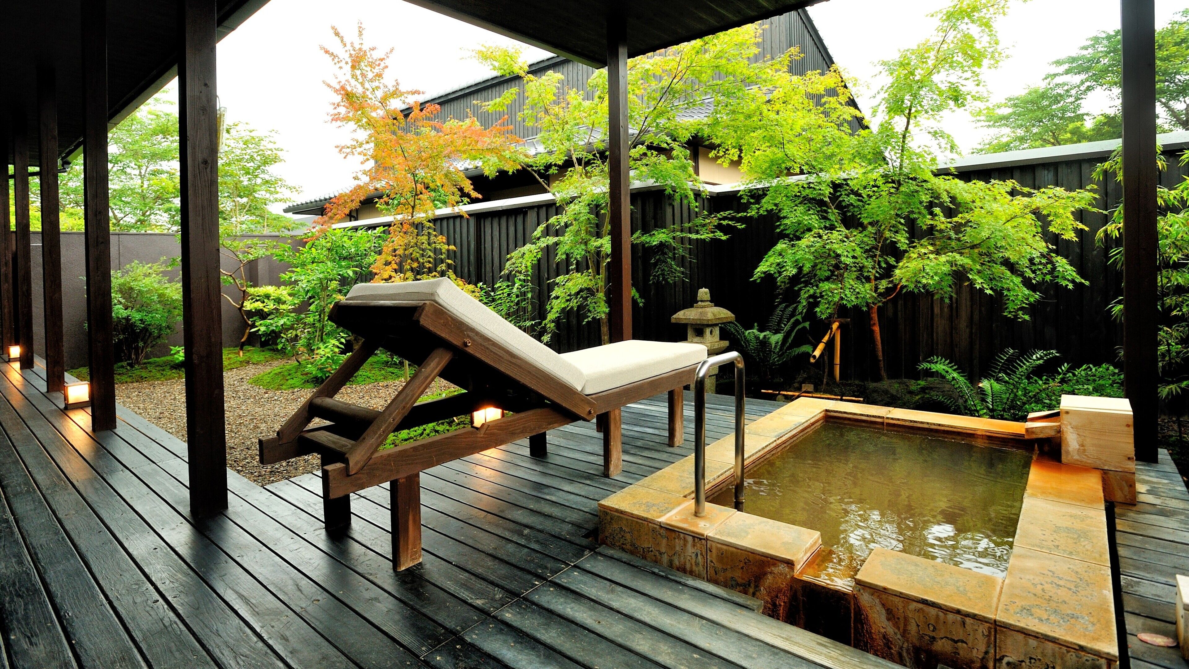 A wooden deck with a hot tub, lounge chair, and stone lantern.