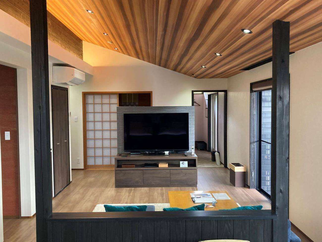 Een moderne woonkamer met een flatscreen televisie op een houten dressoir, een schuifdeur en uitzicht op buiten.