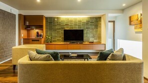 Una sala de estar con un sofá, un televisor de pantalla plana, un mueble de madera y una pared con azulejos verdes.