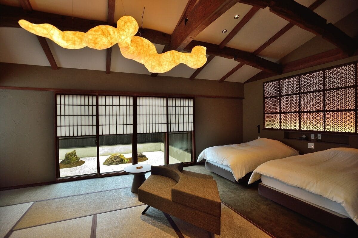 Quarto japonês tradicional com tatames, cama de madeira baixa, um banco acolchoado e um grande biombos shoji.