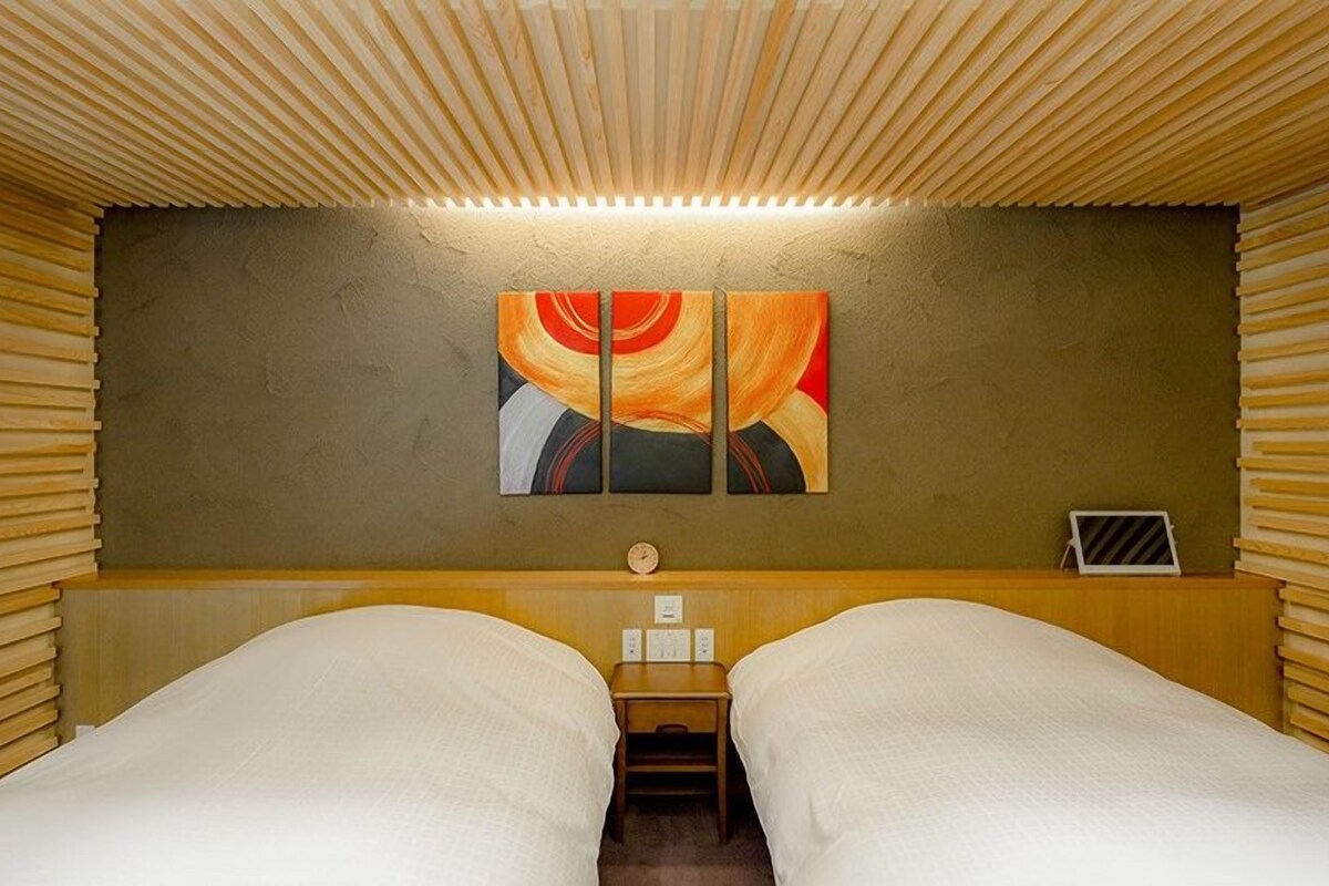 Una stanza con due letti, un soffitto in legno a listelli, una sveglia a muro e un quadro.