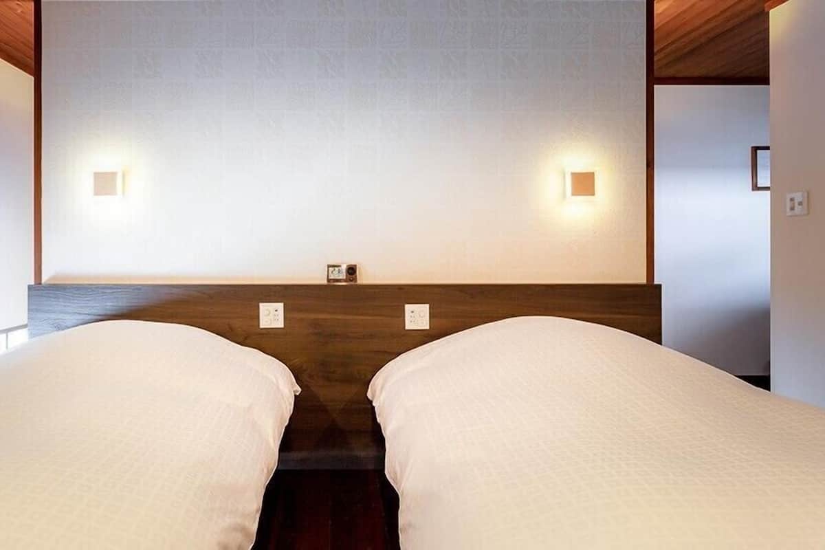 Quarto com duas camas, cabeceira de madeira e luminárias fixadas na parede.