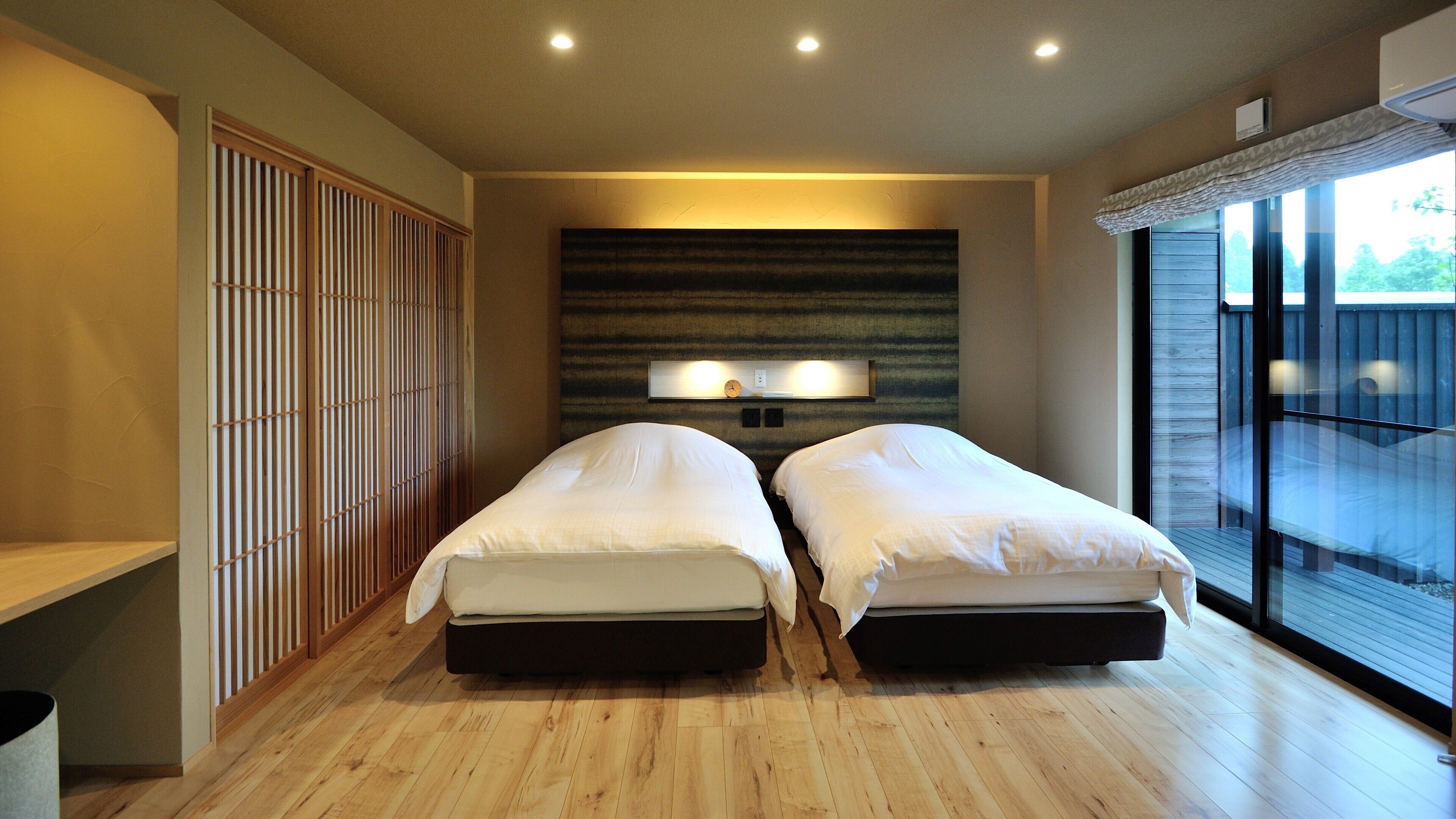 A modern bedroom with two beds, a large window, and a wooden floor.