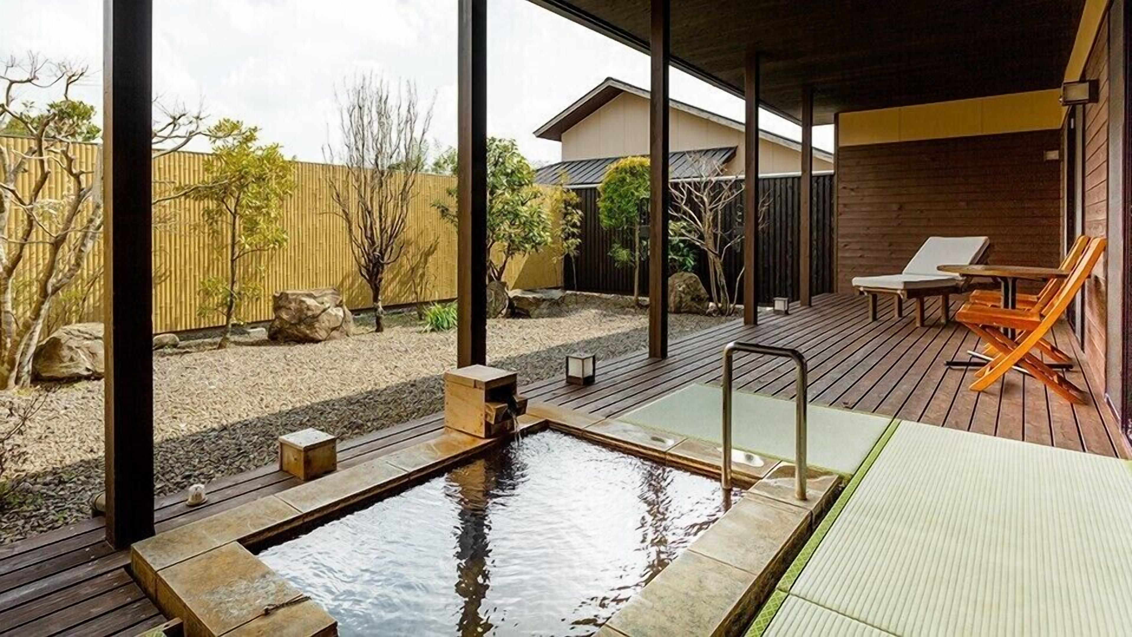 A wooden deck with a hot spring, outdoor seating, and a view of a residential area.