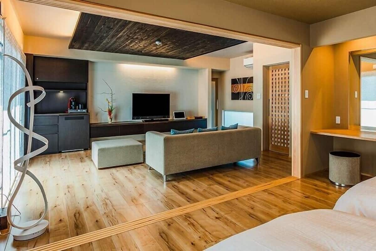 Quarto moderno com sofá, TV e pequena cozinha.