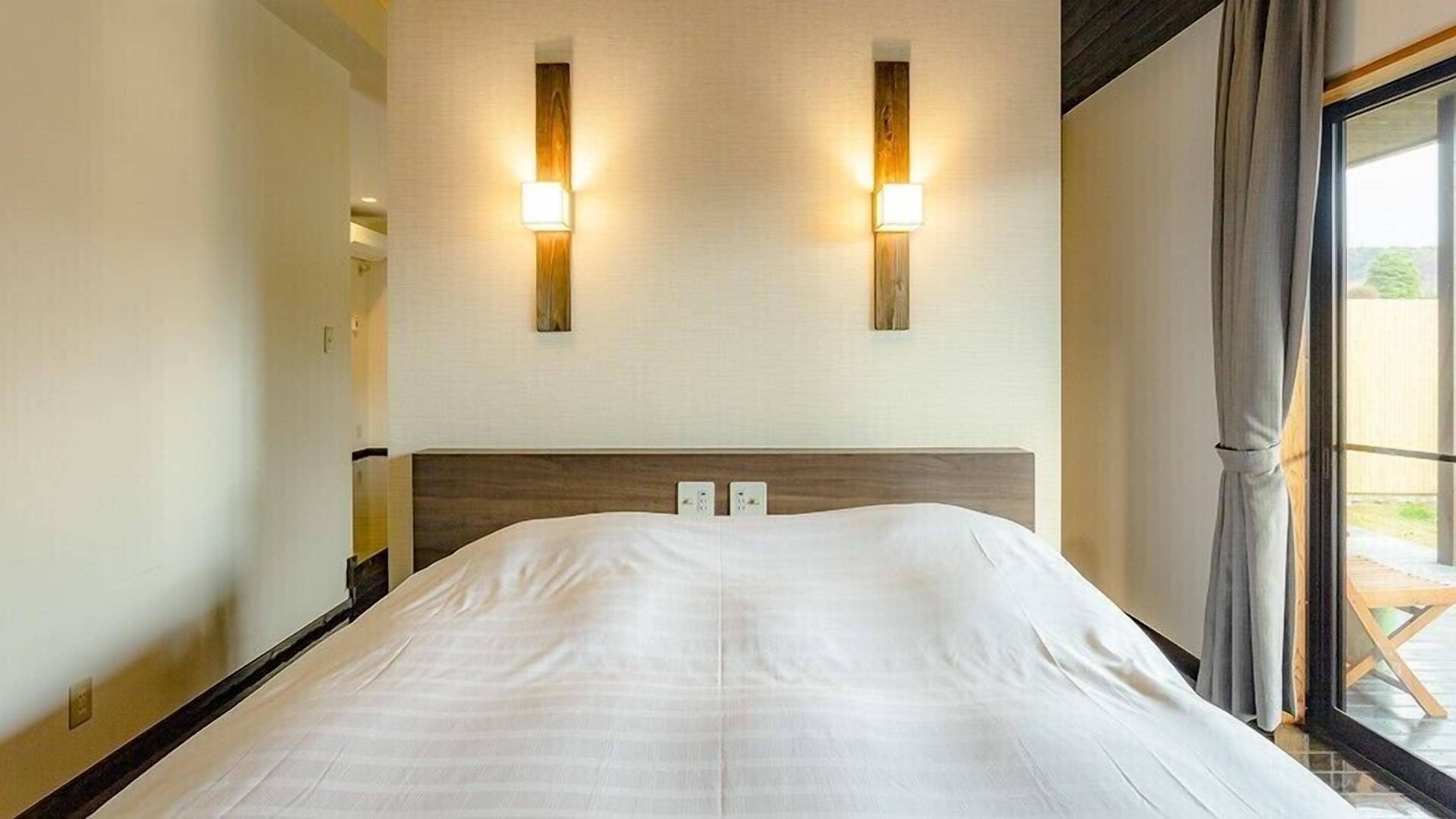 Ein Hotelzimmer mit einem großen Bett, zwei Wandlampen und einem Fenster mit Vorhängen.