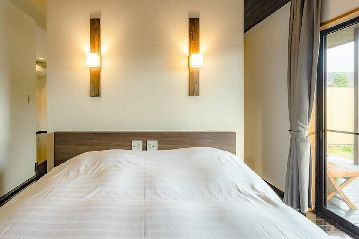 Quarto de hotel com uma cama grande, duas luminárias fixadas na parede e uma janela com cortinas.
