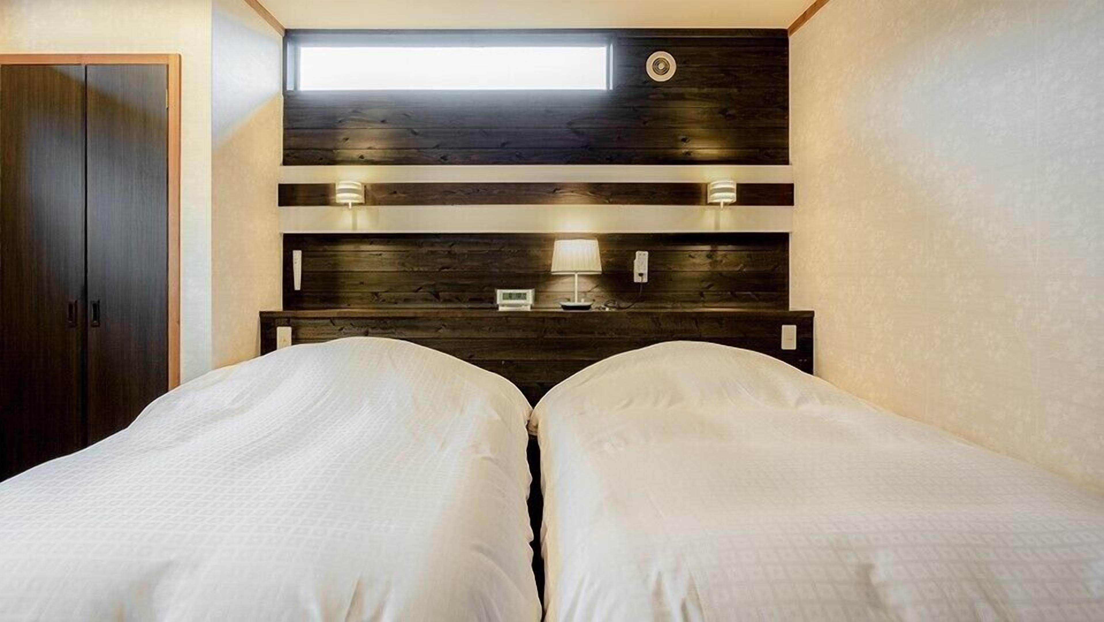 Ein Schlafzimmer mit zwei Betten, einem Oberlicht, einem hölzernen Kopfteil und Nachttischlampen.